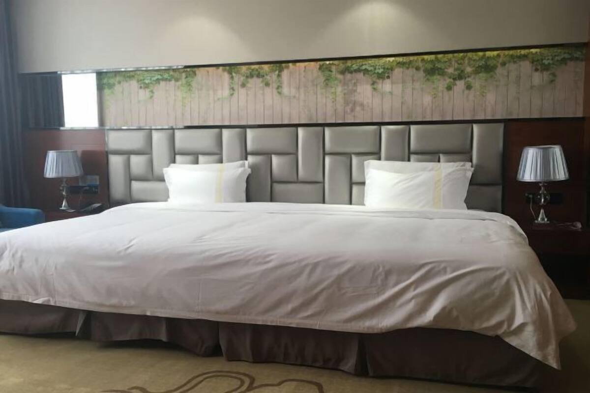 A hotel room with a large bed, a headboard with a textured design, and a wall-mounted artwork.