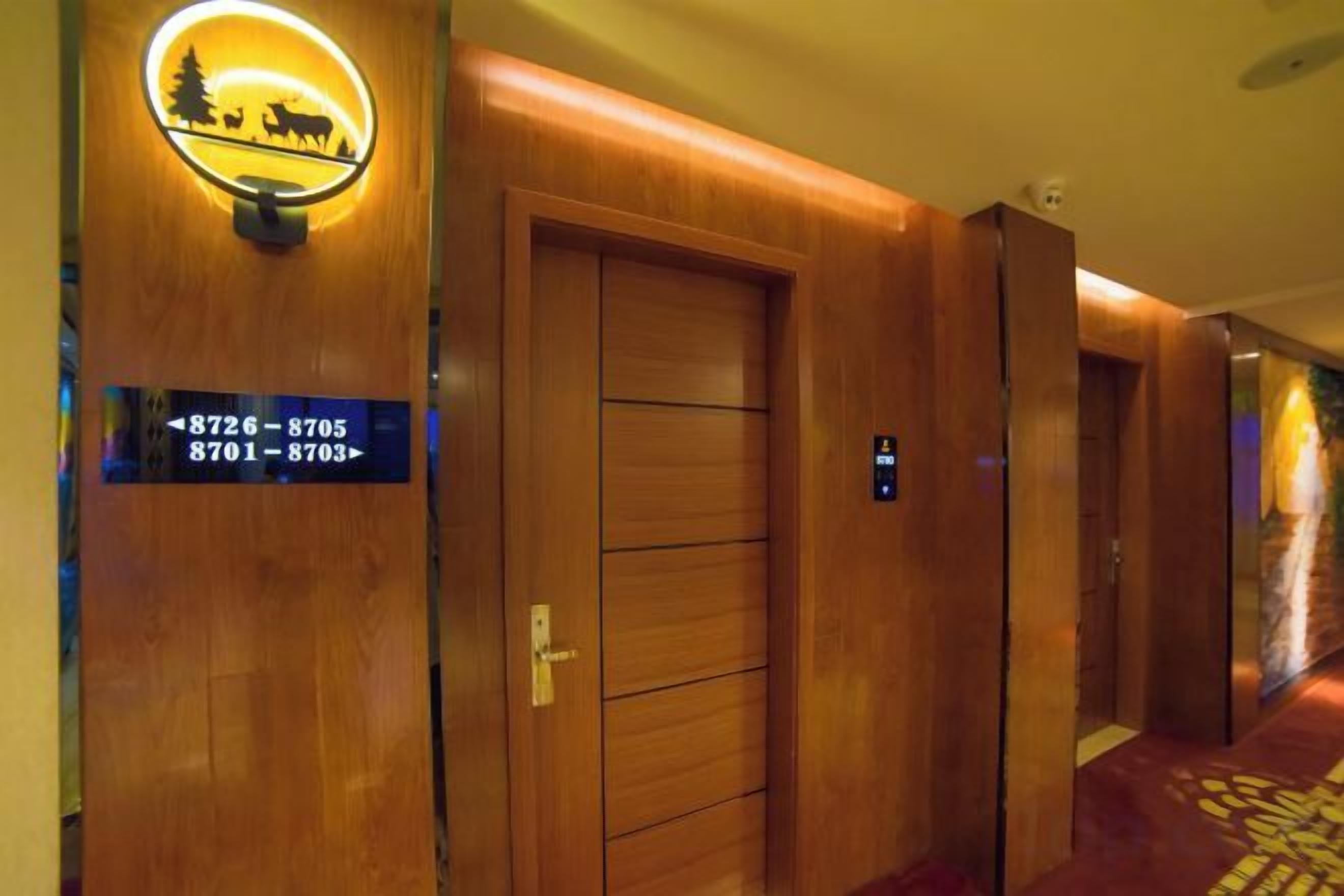 A hotel hallway with wooden doors, a sign with room numbers, and a carpeted floor.
