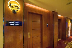 Un pasillo de hotel con puertas de madera, un cartel con números de habitaciones y piso alfombrado.