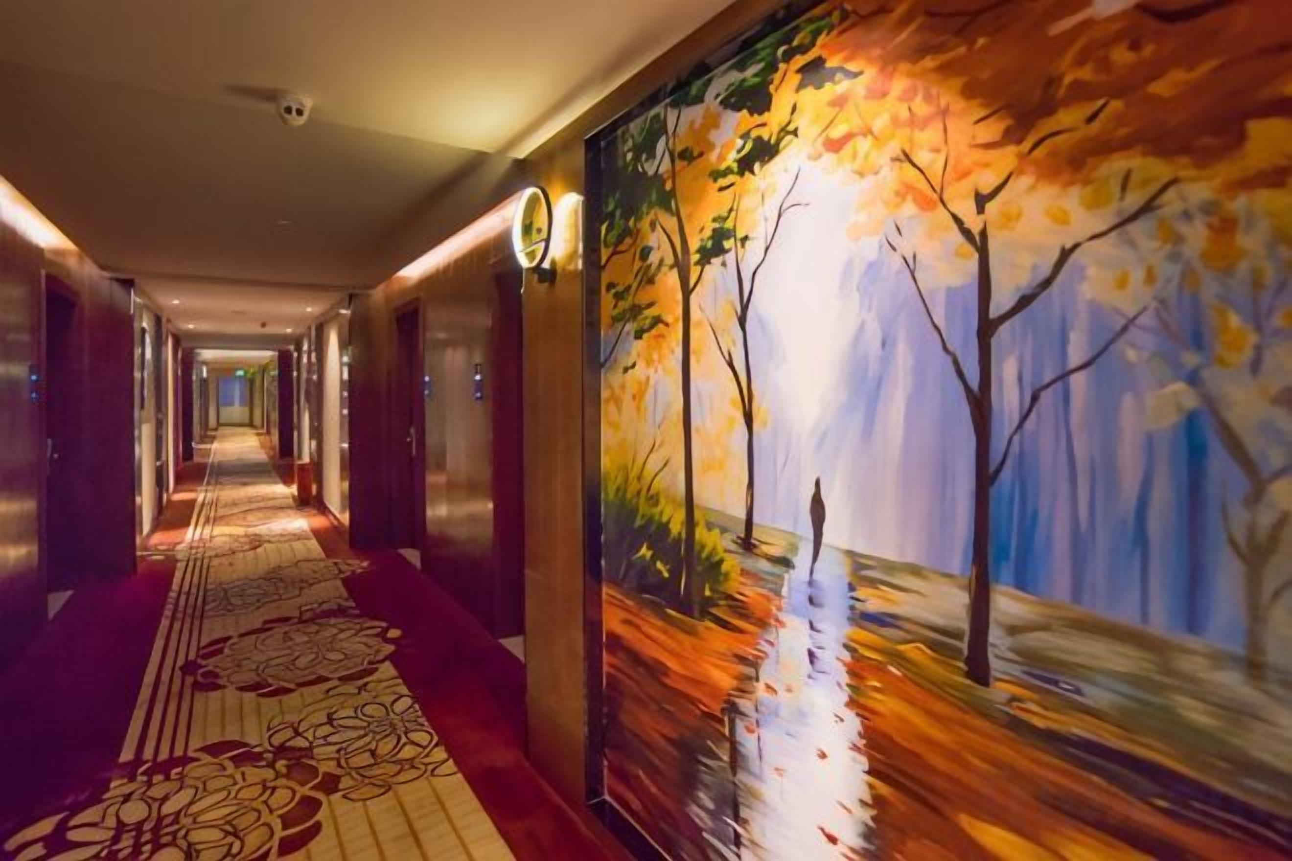 A hotel corridor with a long hallway, carpeted floor, and a mural on the wall depicting a tree and a reflective surface.