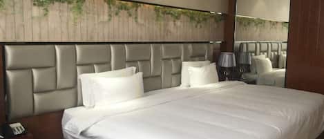 Habitación de hotel con una cama grande, cabecera con diseño texturizado, mesita de noche con lámpara y espejo instalado en la pared.