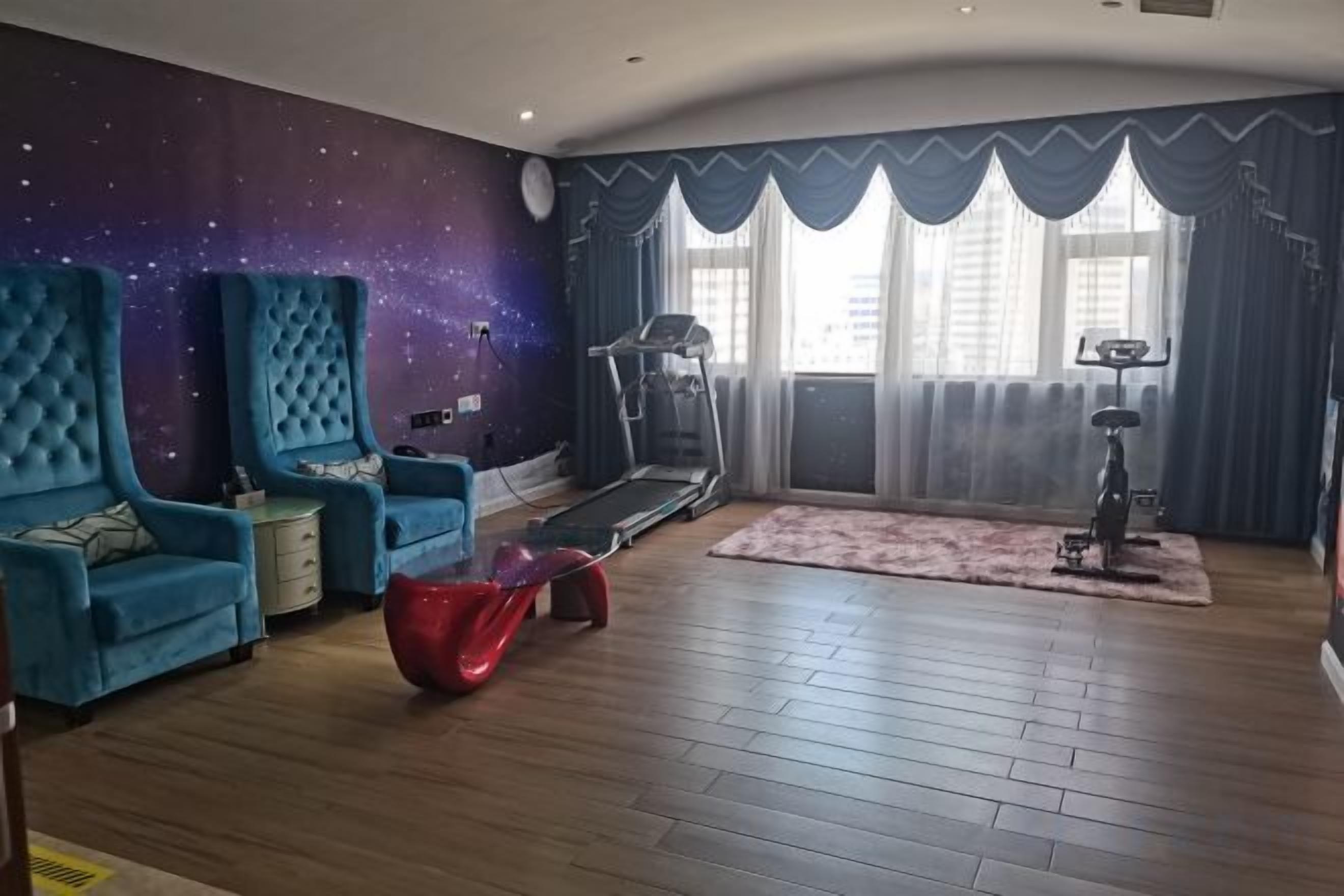 A room with a treadmill, a large blue chair, a red bean bag, and a starry wall mural.