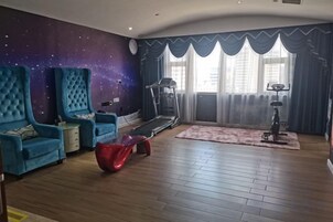 Una habitación con una cinta de correr, un sillón azul grande, un asiento de peluche rojo y un mural de estrellas en la pared.