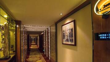 A hotel hallway with a carpeted floor, framed artwork on the walls, and a door with a number sign.