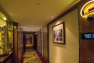 Un pasillo de hotel con piso alfombrado, cuadros en las paredes y una puerta con un número.