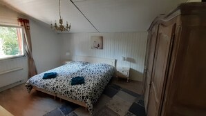 Quarto com cama, mesa de cabeceira, cômoda, lustre e janela com cortinas.