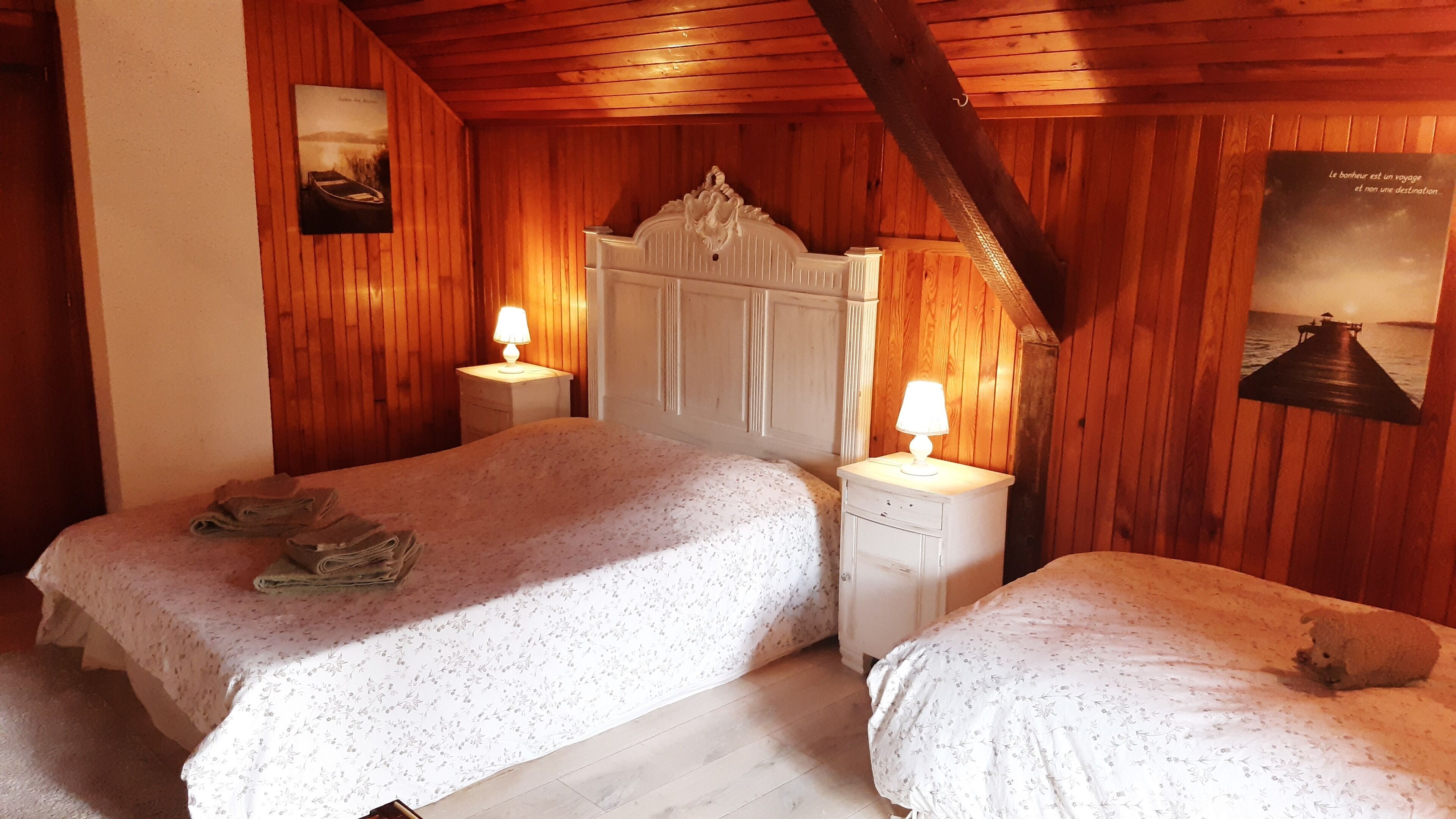 Une chambre chaleureuse avec deux lits, des murs en bois, une tête de lit blanche et une affiche accrochée au mur.