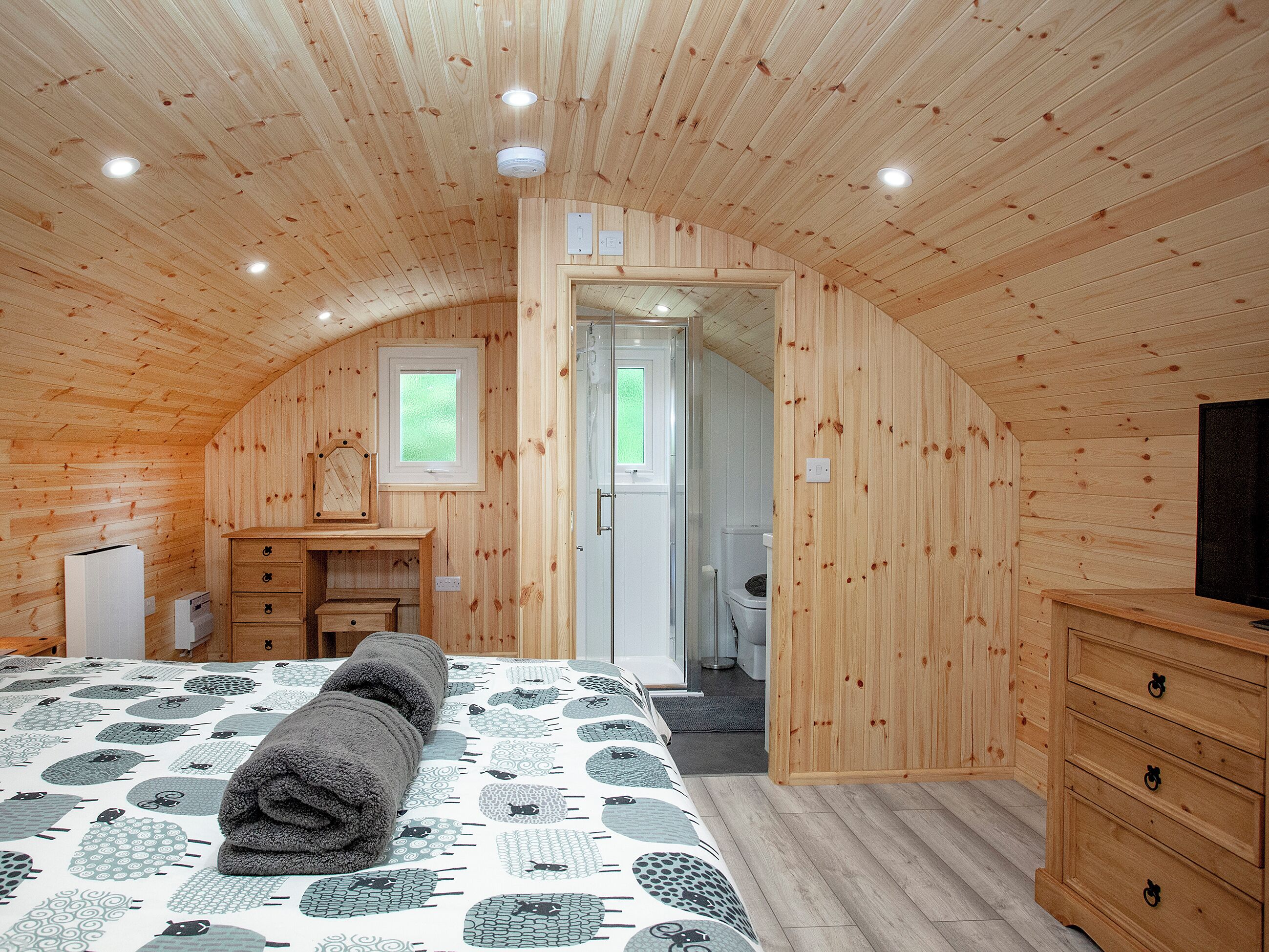 A cozy bedroom with a wooden ceiling, a bed with a patterned bedspread, a dresser, and a television.