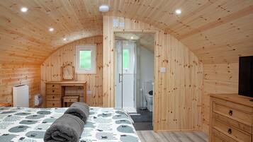 A cozy bedroom with a wooden ceiling, a bed with a patterned bedspread, a dresser, and a television.