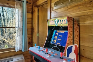 Una máquina recreativa con temática de baloncesto, una ventana con cortinas y paredes de madera.