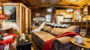 Ein gemütliches Blockhausschlafzimmer mit Holzbalkendecke, einer Couch, einem Esstisch und einer Küchenzeile.