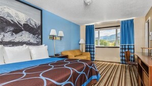 Habitación de hotel con una cama grande, un escritorio, una silla y vistas a las montañas a través de la ventana.