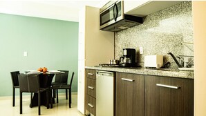A compact kitchen with a microwave, coffee maker, and toaster. There is a dining table with chairs and a small fruit bowl. - Tiny Apartment with Rooftop pool y GYM (Mexico City)
