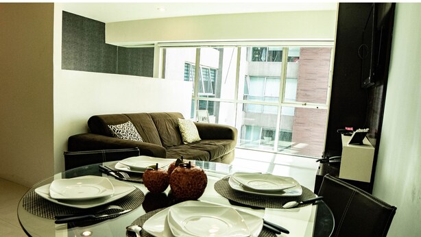 A modern living room with a glass dining table set for four, a brown sofa with patterned cushions, and a large window offering a view of the cityscape. - Tiny Apartment with Rooftop pool y GYM (Mexico City)