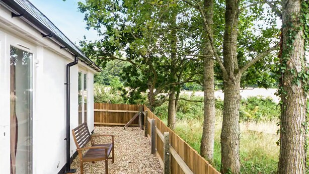 A white building with a wooden bench and a wooden fence in a garden area.