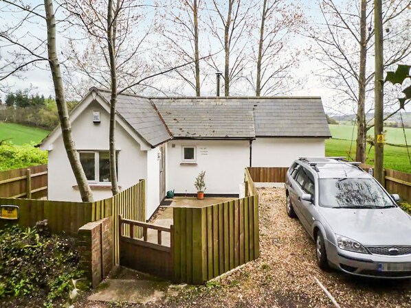 A white house with a sloped roof, a fenced garden, and a parked car. - The Old Telephone Exchange (Mamhead, near Starcross)