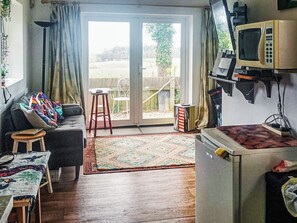 A living room with a sofa, a small stool, a table, a patterned rug, and a sliding glass door leading to an outdoor area. - The Old Telephone Exchange (Mamhead, near Starcross)