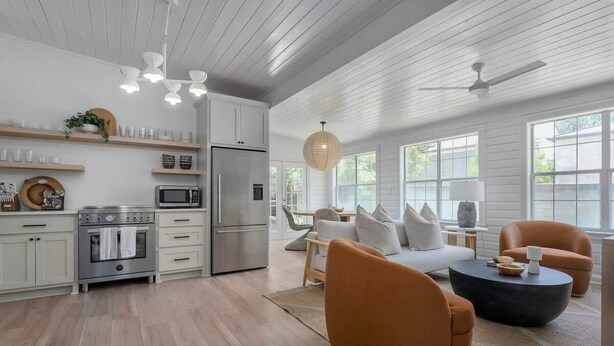 A spacious kitchen with white cabinetry, a microwave, and a stove. There are two orange chairs and a black coffee table. - The Ressman Haus at MarktPlatz, Walk to Main St! (Fredericksburg)