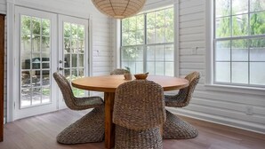 A dining area with a round wooden table and woven chairs, large windows, and a hanging light fixture. - The Ressman Haus at MarktPlatz, Walk to Main St! (Fredericksburg)