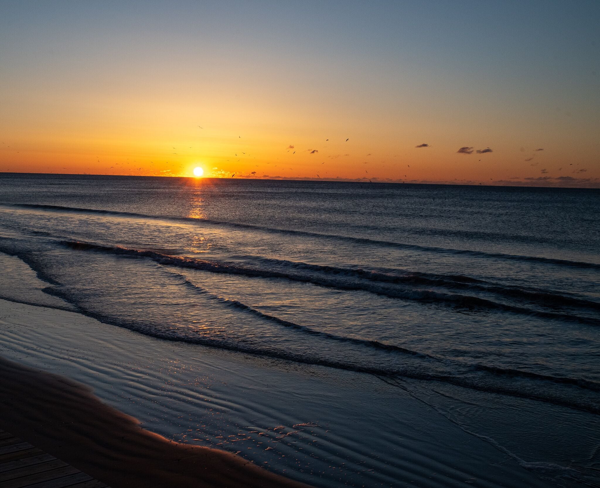 Ein Sonnenuntergang über dem Meer, Wellen nähern sich dem Strand.