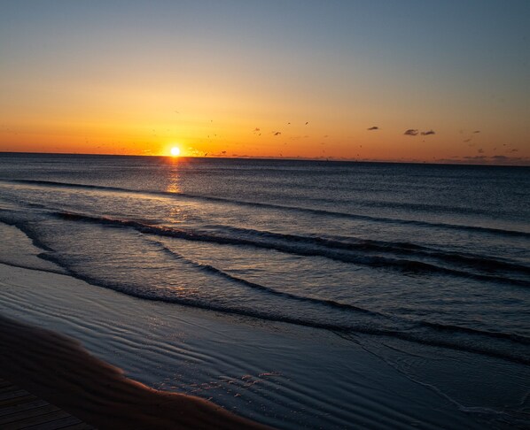 A sunset over the ocean with waves approaching the shore.