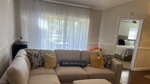 Un salon avec un canapé d’angle beige, un pouf assorti et une petite table d’appoint sur laquelle est posée une plante.