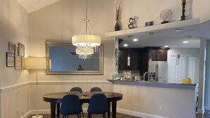 Un coin repas agrémenté d’un lustre, une table à manger avec des chaises, un miroir et, au fond, une cuisine.