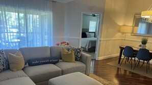 Un salon avec un canapé d’angle gris, un pouf et un coin repas comprenant une table et des chaises.