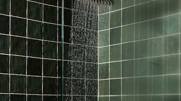A showerhead with water flowing down a tiled wall.