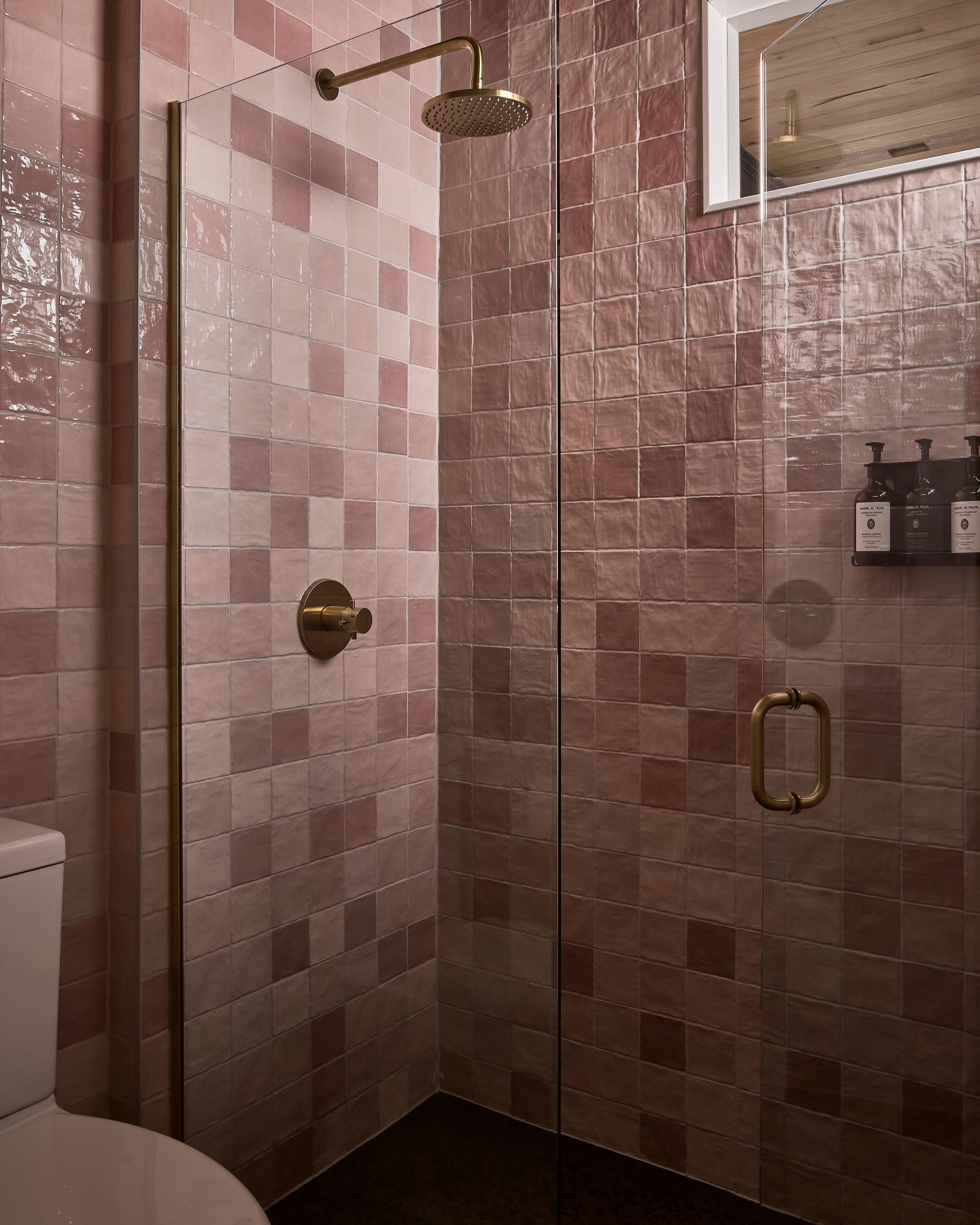 A bathroom with a glass shower enclosure, a toilet, and a sink with toiletries.