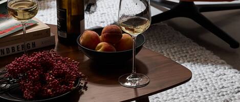 Une table avec une bouteille de vin, deux verres, un saladier de fruits et des livres.