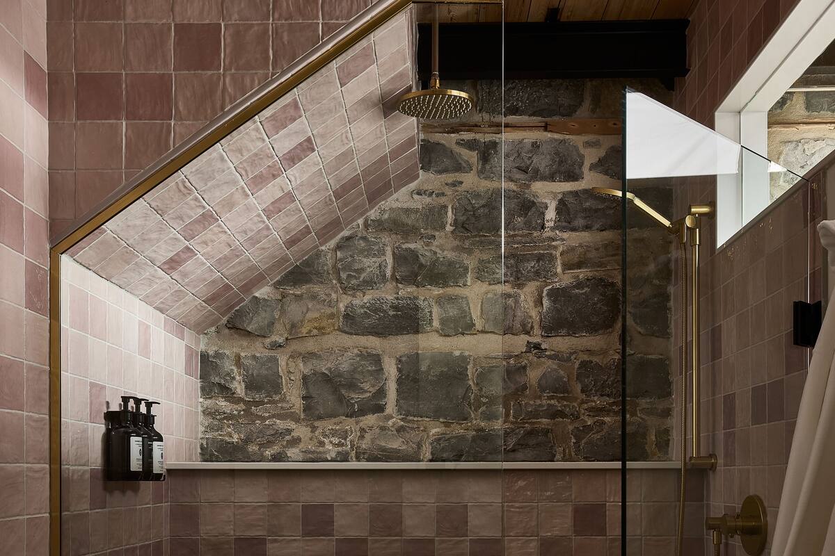 Un baño con pared de piedra, ducha con cabezal dorado y retrete.