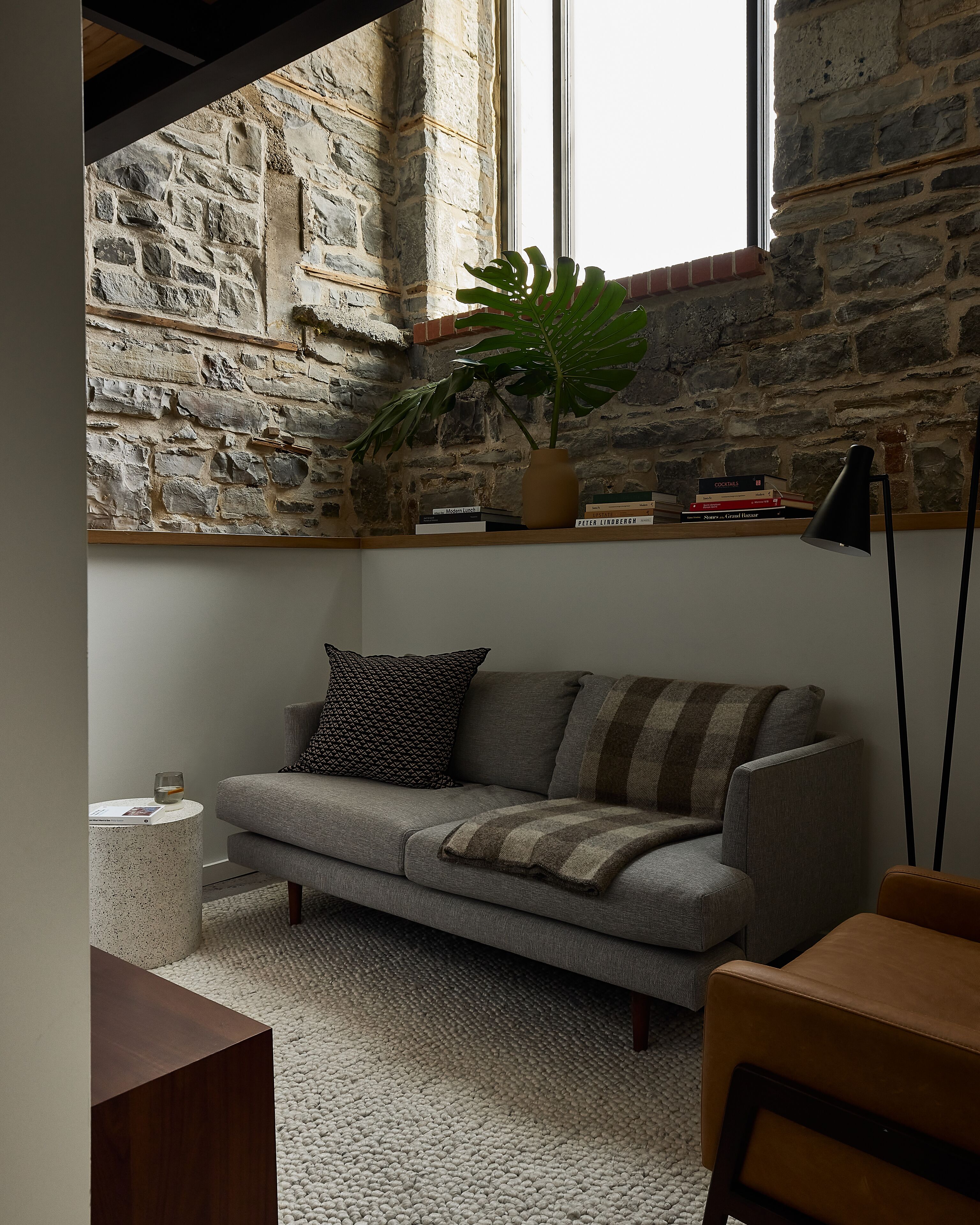 Una sala de estar acogedora con una pared de piedra, un sofá gris, una planta en maceta y una estantería.