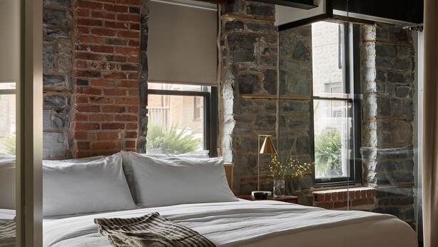 A bedroom with a large bed, a brick wall, and a window with a view of the outside.