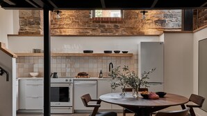 A modern kitchen with white cabinets, a stone accent wall, and a dining area with a round table and wooden chairs.