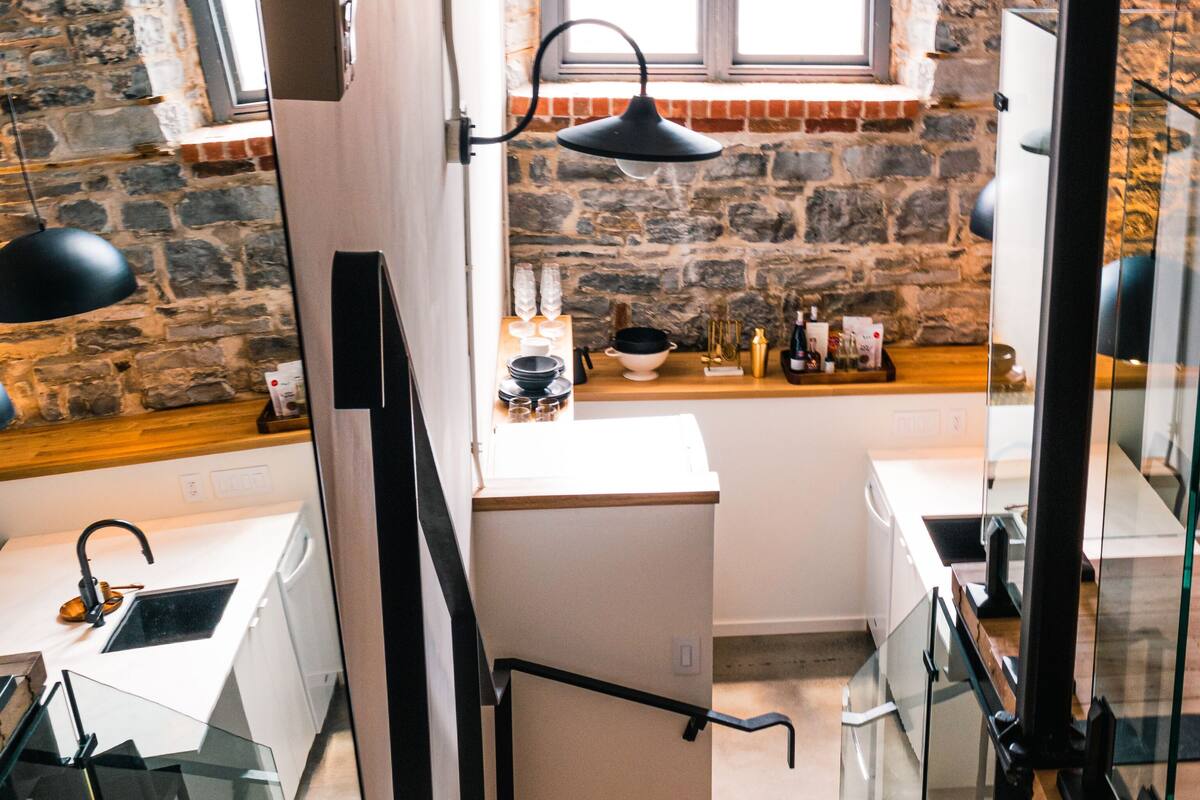 Una cocina con pared de piedra, una ventana, un lavamanos y una encimera con diversos objetos.