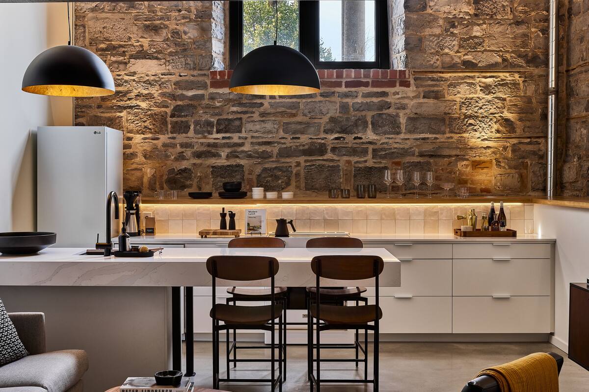 Una cocina moderna con pared de piedra, una isla blanca con taburetes de bar y un refrigerador LG grande.