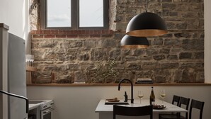 A kitchen with a stone wall, a window, a dining table with chairs, and a hanging light fixture.