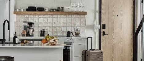 A modern kitchen with a central island, a dining area with wooden chairs, and a suitcase on the floor.