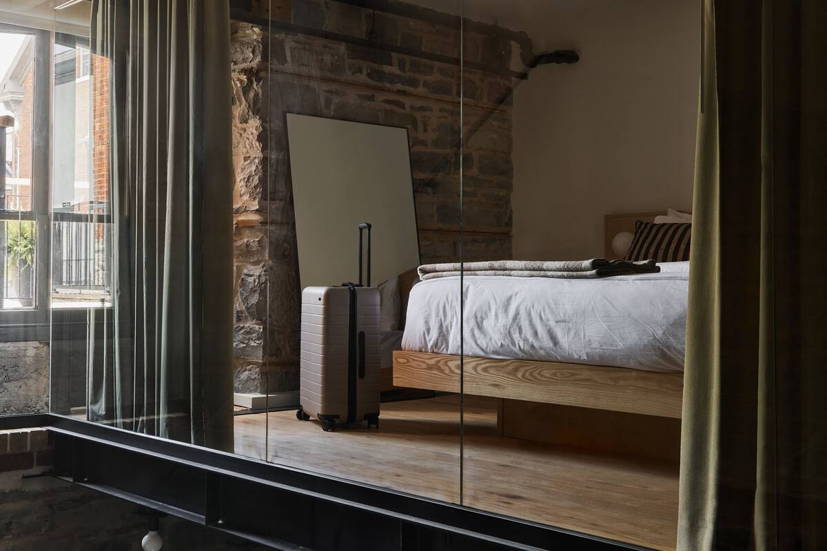 Un dormitorio moderno con una cama grande, una maleta y un espejo sobre suelo de madera.