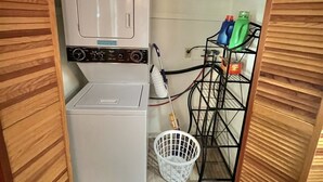 A compact laundry room with a washer and dryer, a metal rack with cleaning supplies, and a white laundry basket. - Great Place for a Family Retreat! Sleeps 10 (Naples)