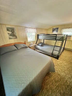 A room with a bunk bed, a single bed, a small round table, and two framed pictures on the walls.