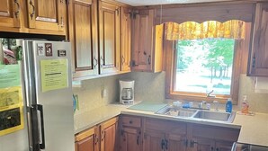 A kitchen with wooden cabinets, a refrigerator, a coffee maker, and a window with a view of trees. - Great Place for a Family Retreat! Sleeps 10 (Naples)