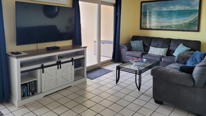 Una sala de estar con televisor de pantalla plana, un sofá, una mesa de centro y un balcón con vista al océano.