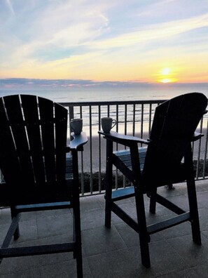 Deux fauteuils Adirondack sur un balcon, avec vue sur le coucher de soleil sur l’océan.