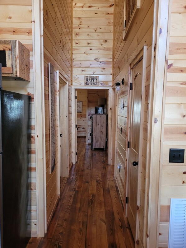 Interior de una cabaña de madera con un pasillo central que conduce a una zona de cocina.
