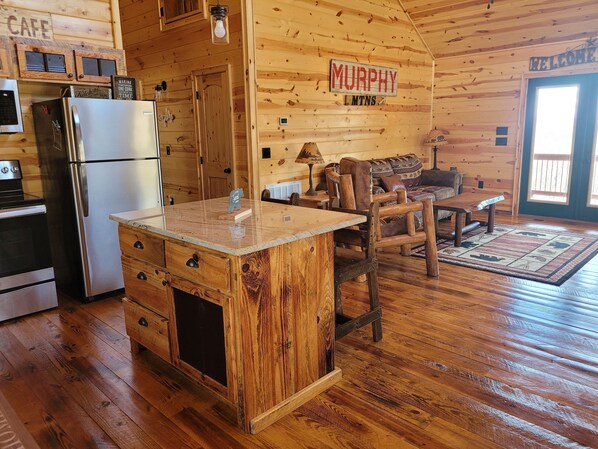 A cozy cabin interior with a wooden interior, a kitchen with a stainless steel refrigerator, a wooden dining table, and a sofa.