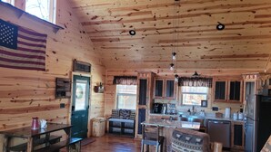 A rustic cabin interior with wooden walls and ceiling, a dining area with benches, a kitchen with wooden cabinets, and a large American flag. - Mountain View Cabin,15 Min to Casino, Family Friendly (murphy)