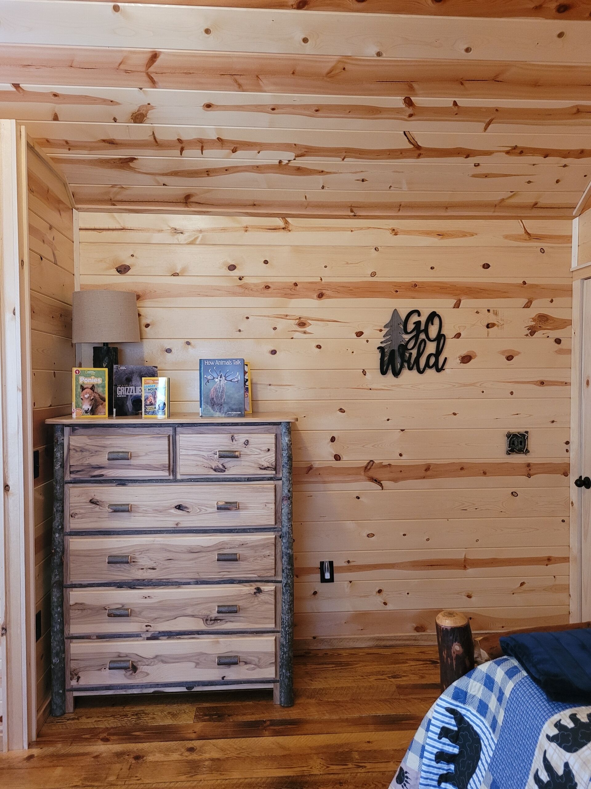 Une pièce rustique en bois, avec une commode, un mur orné d’une affiche « Laissez libre cours à votre imagination » et une lampe.