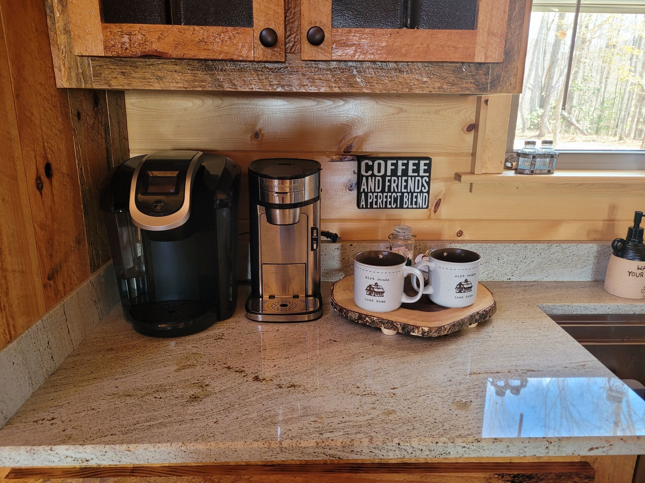 A kitchen with a coffee maker, two mugs, and a sign that reads "Coffee and Friends a Perfect Blend".